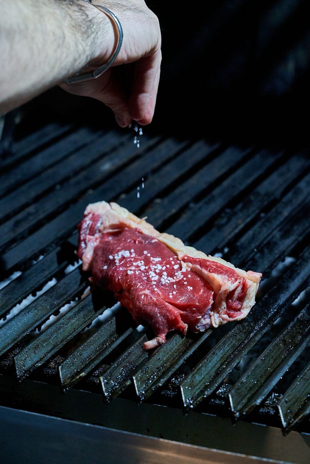 El parrillero salando un bife sobre la parrilla
